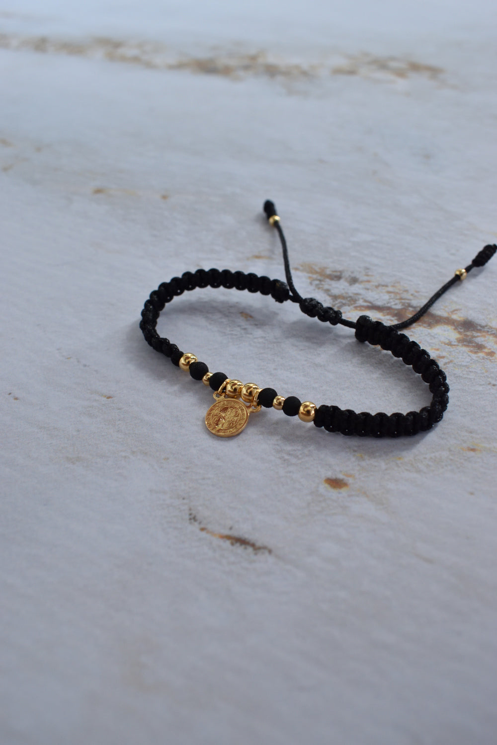 Pulsera de protección San Benito negra y dorada con empaque premium Pólux