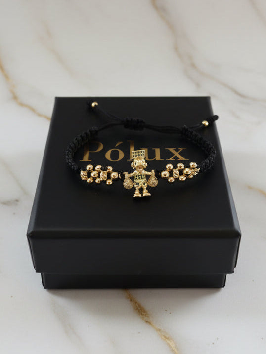 Detalle en ángulo del dije Tío Rico en oro laminado 18K sobre pulsera de macramé